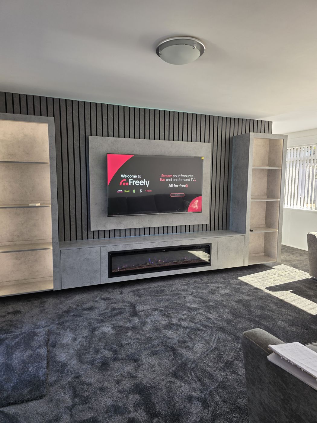 Ayrshire media wall with grey concrete panel, black slats, open display shelving either side and a long electric fire.