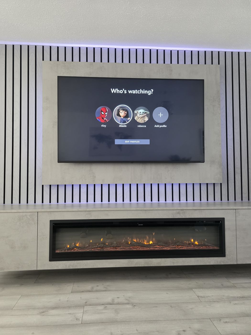 Edinburgh media wall with light grey concrete panel, grey oak slats, purple LED lighting and a long electric fire.