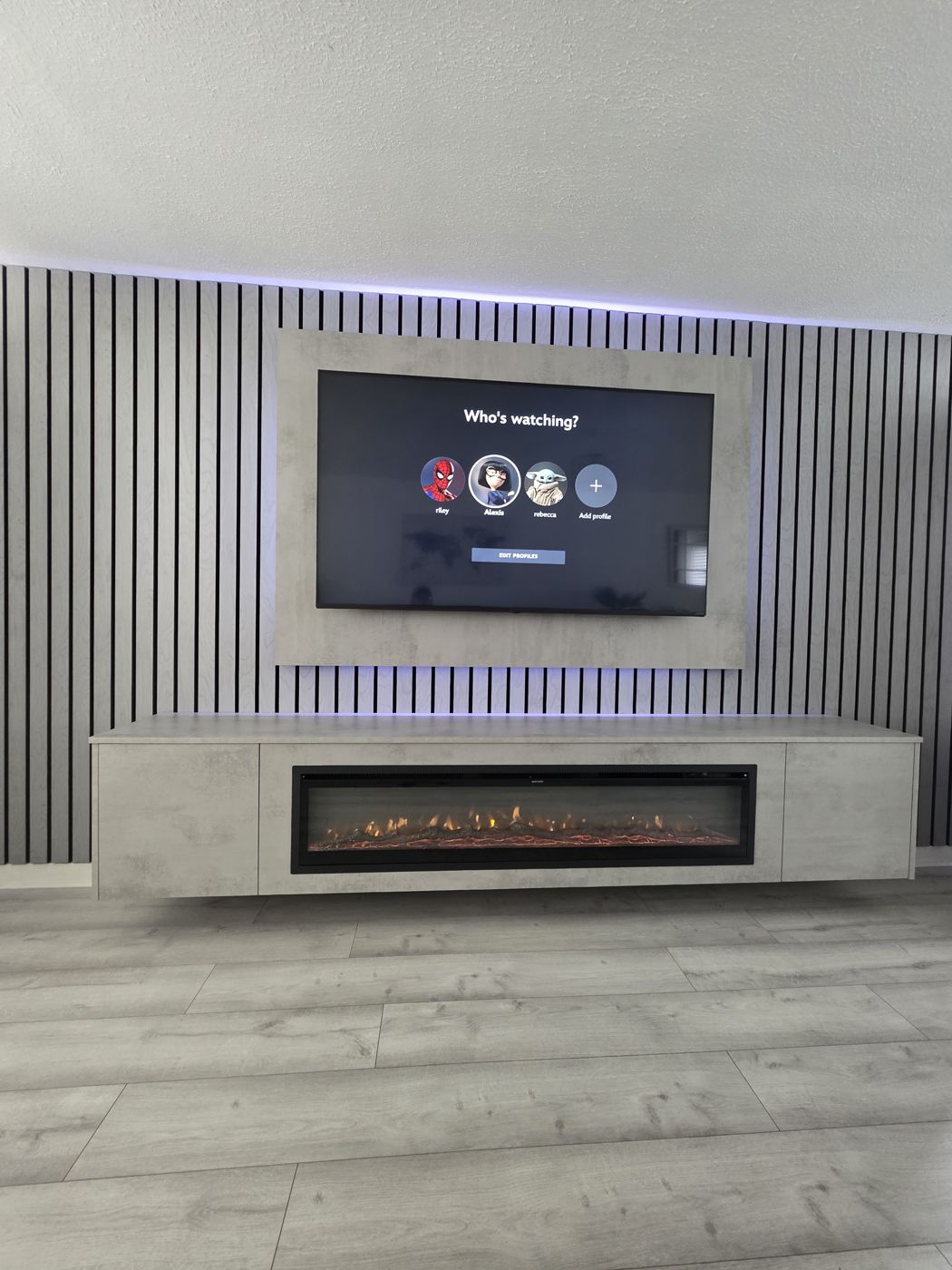 Wide Edinburgh media wall with grey oak slats, light grey concrete panel, purple LED lighting and electric fire.