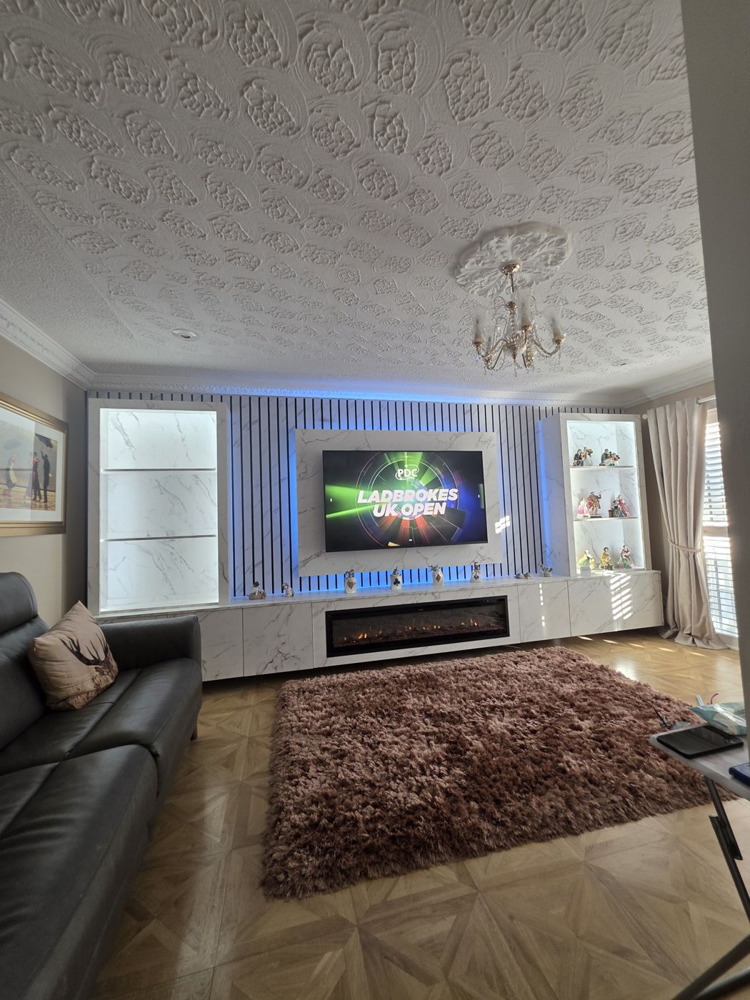 Falkirk media wall with a white marble panel, black slats, blue LED, glass display cabinets either side and an electric fire, by MPS Media Walls.
