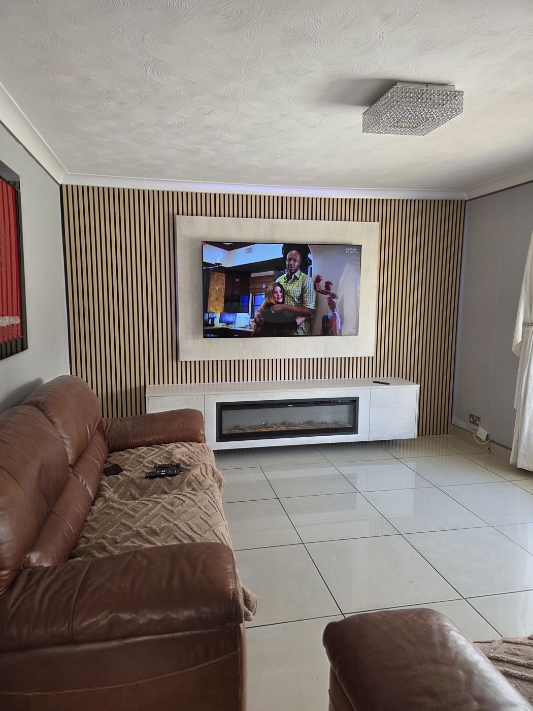 Lanarkshire media wall with a cream concrete panel, oak slats and a long floating cabinet with an electric fire below the TV, by MPS Media Walls.