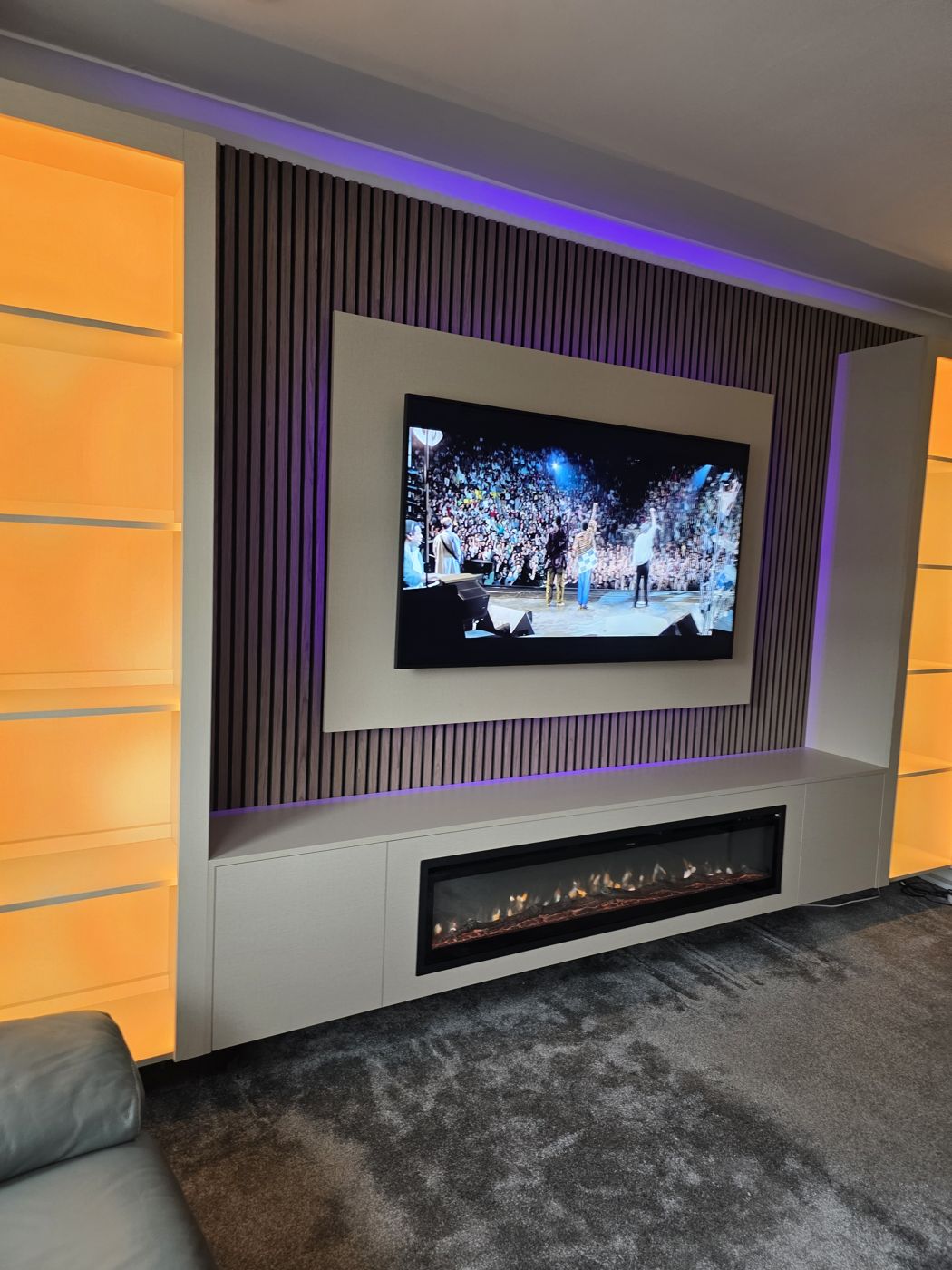 Lanarkshire media wall, cream panel, dark oak slats, purple LED, amber-lit display cabinets either side and electric fire.