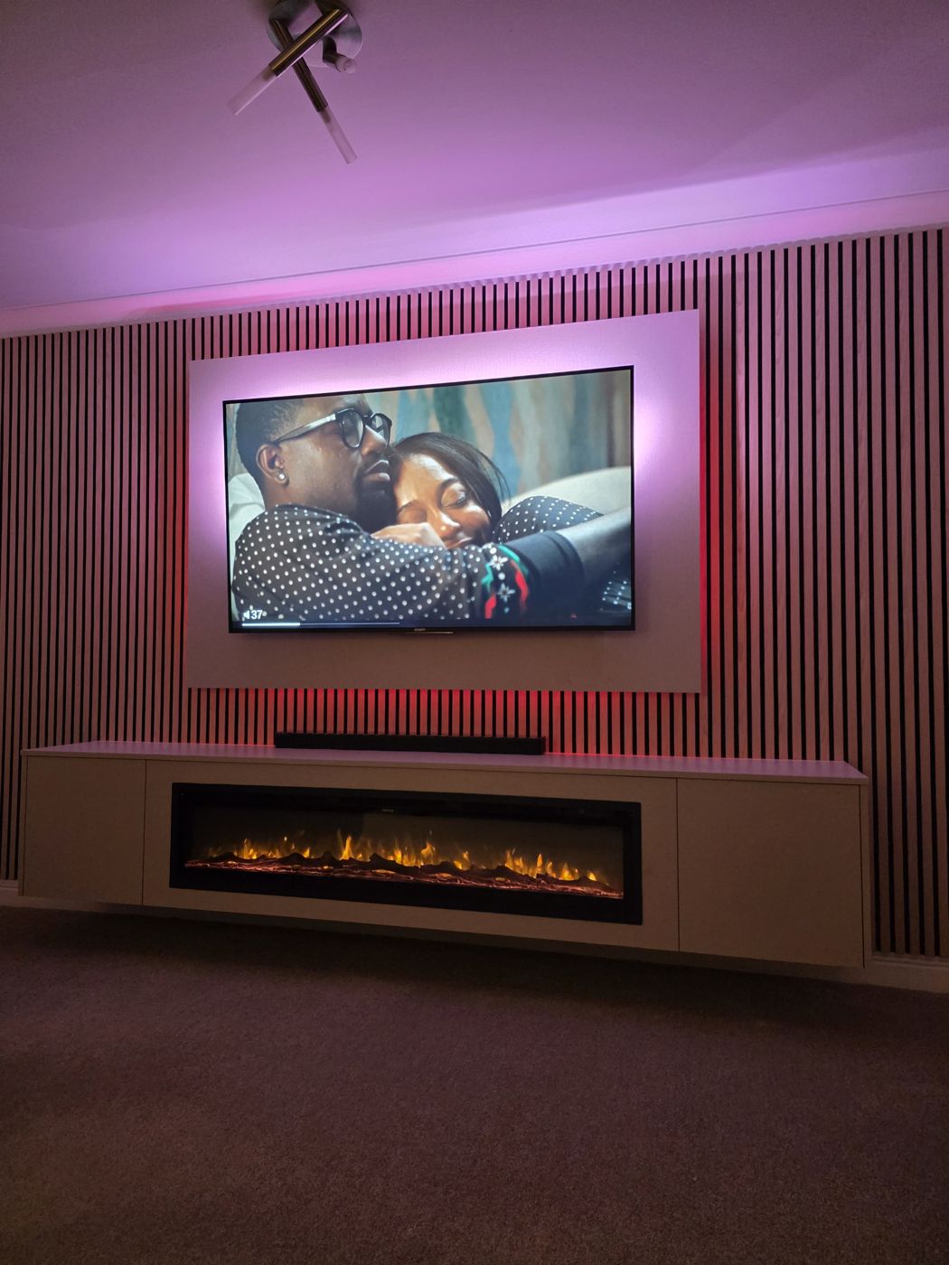 Paisley media wall with cream TV panel, dark charcoal slat wall, wide black electric fire and vivid pink LED backlighting