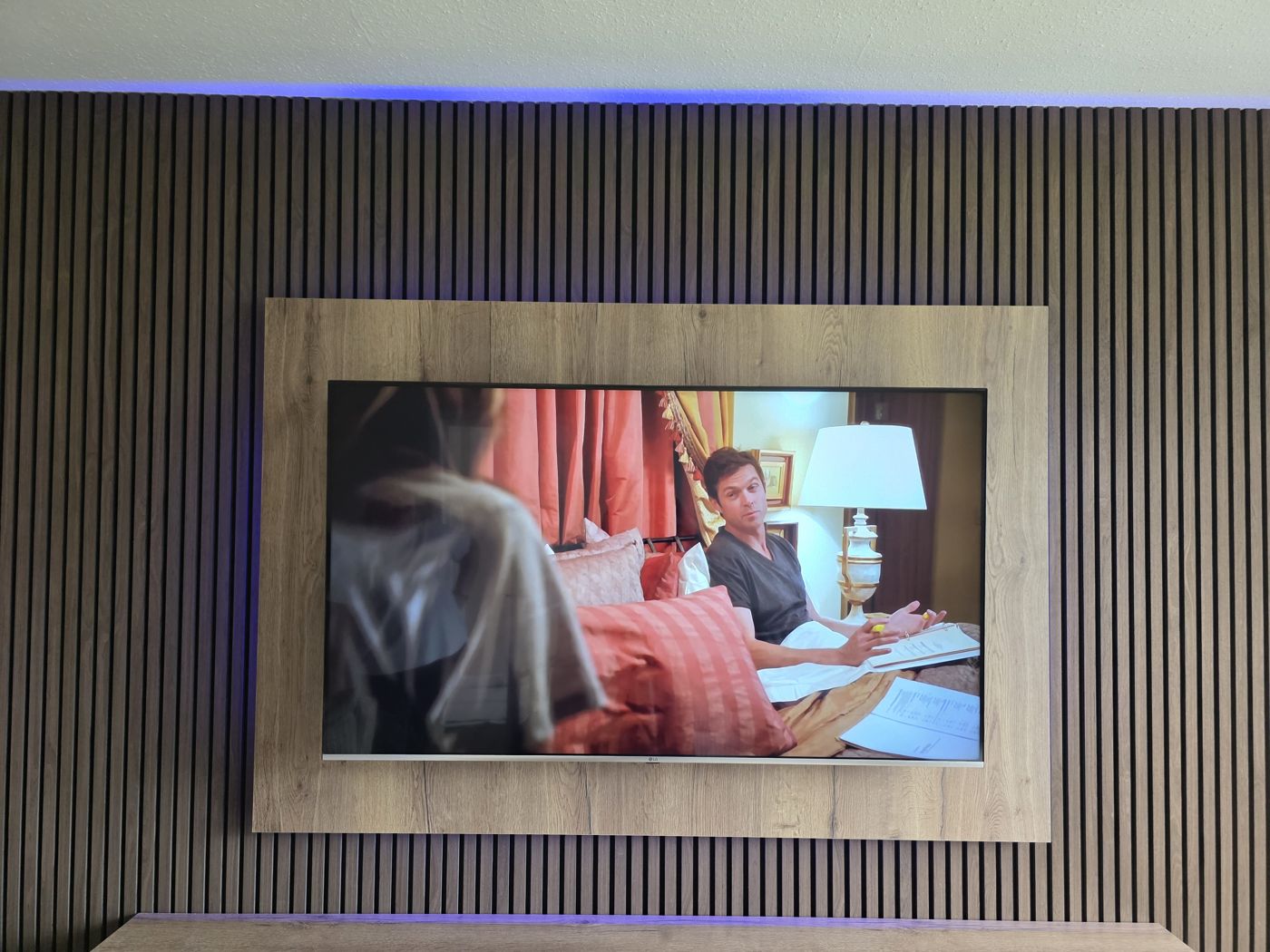 Light oak TV panel framing the screen on a full charcoal slatted wall with a purple LED glow, fitted in Stirling, by MPS Media Walls.