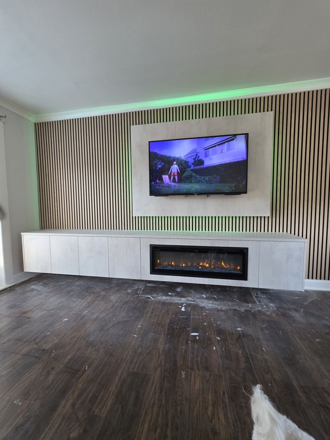 Cream TV panel on oak slatted wall with green LED and white cabinet with long electric fire, West Lothian.