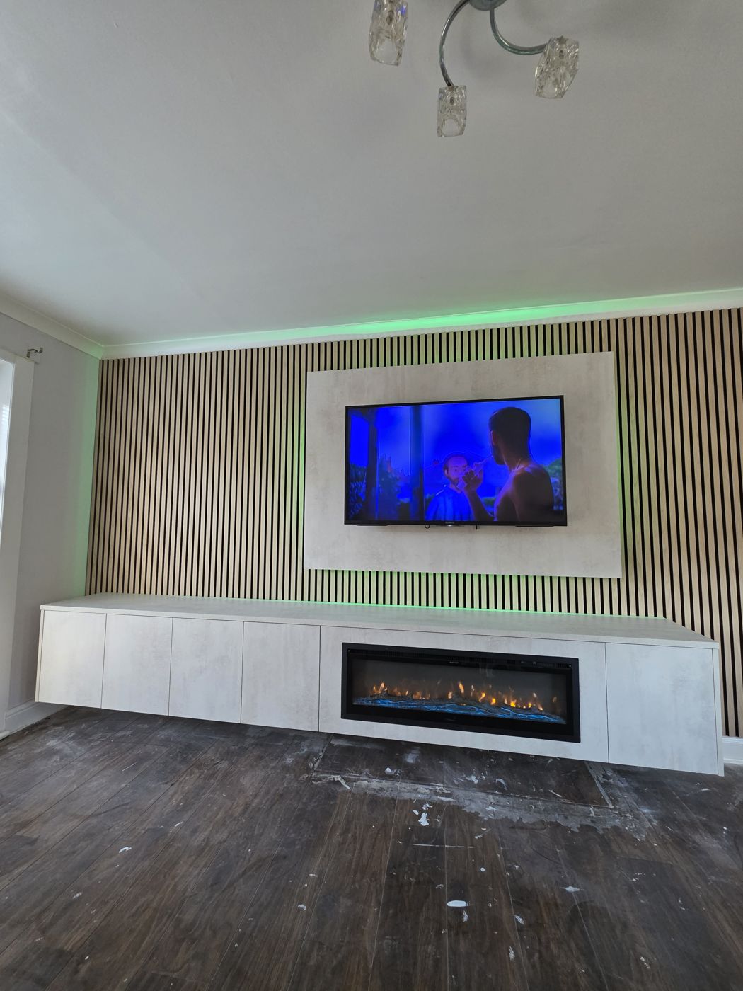 Full-wall oak slats with green LED frame a cream TV panel and white cabinet with electric fire, West Lothian.