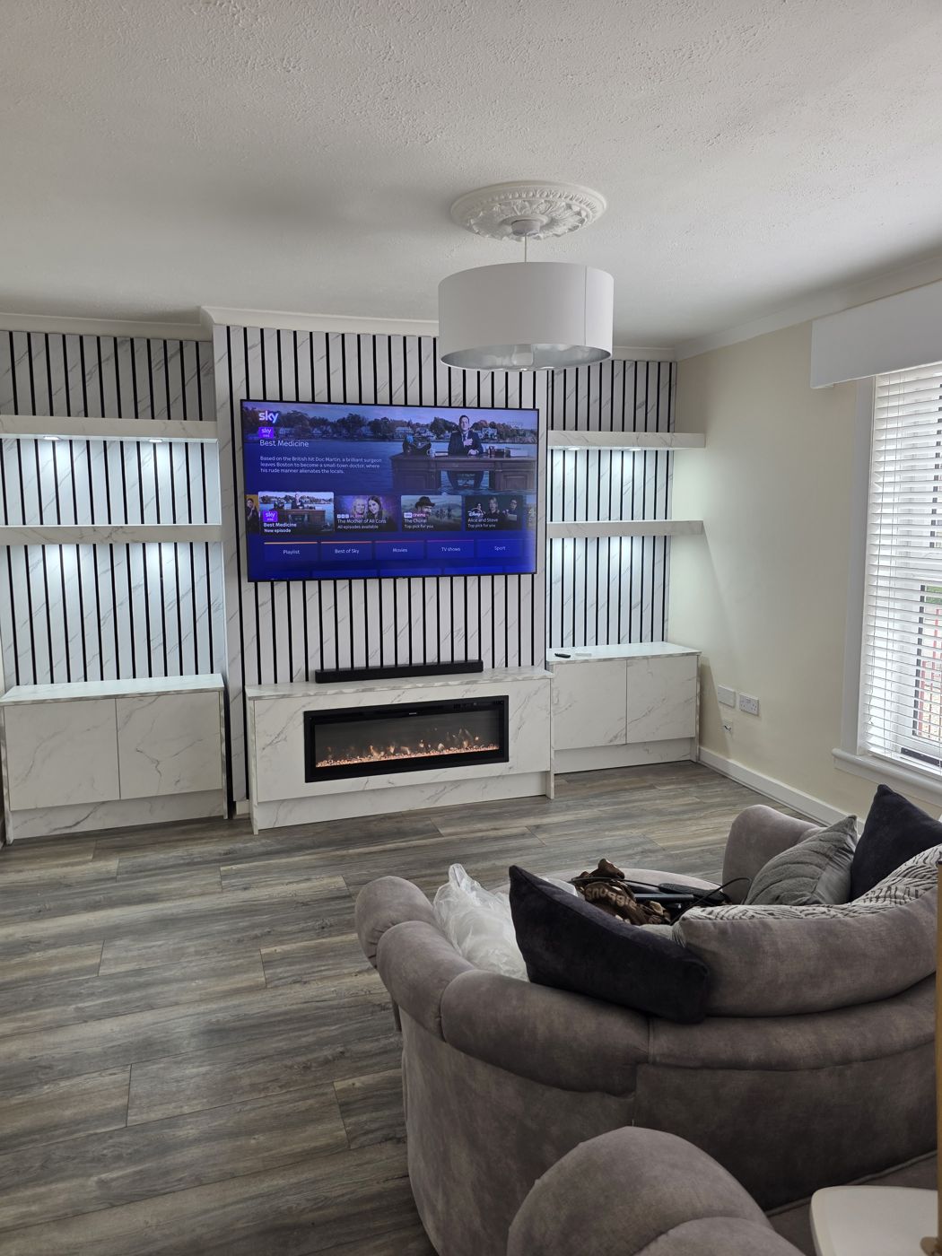 White marble TV panel, black-and-white slatted wall, lit side shelves and cabinet with electric fire, West Lothian.