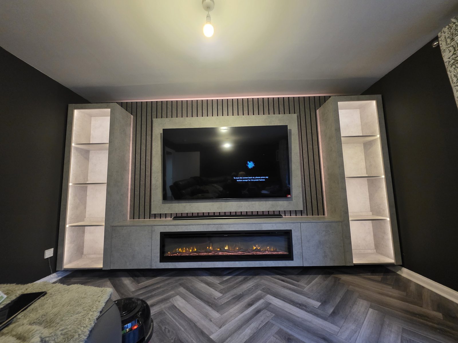 Light grey Chicago concrete media wall fitted in Paisley with tall illuminated display cabinets, an electric fire and grey herringbone flooring, by MPS Media Walls.