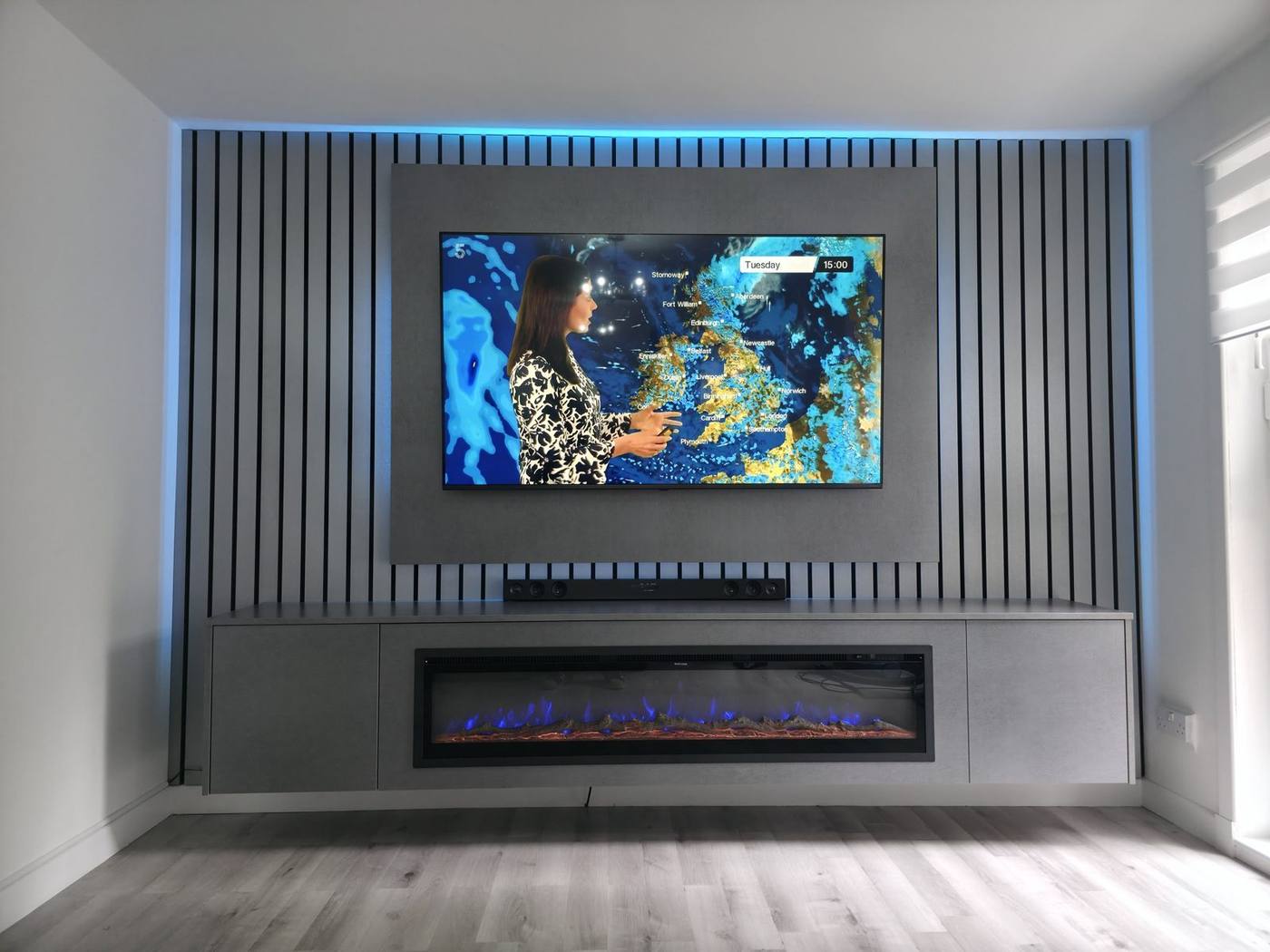 Grey slatted media wall with blue LED halo, soundbar and panoramic electric fire