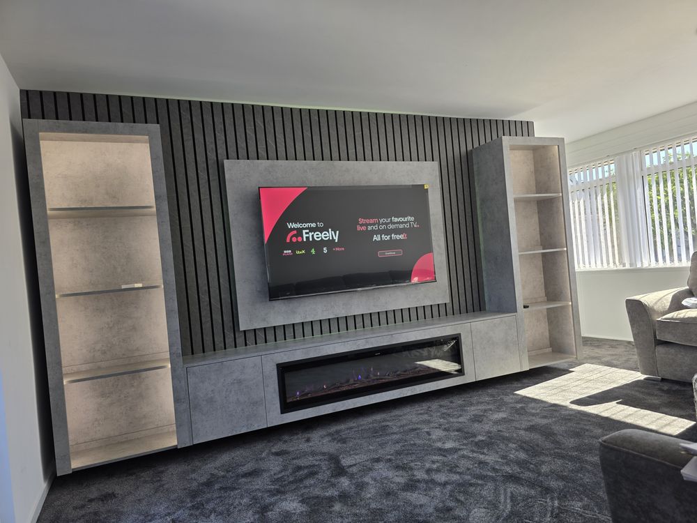 Angled view of Irvine light grey Chicago concrete media wall, lit shelving units flanking the TV above a linear electric fire, by MPS Media Walls