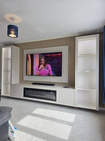 Cream built-in media wall with oak slats, shelving and slim electric fire